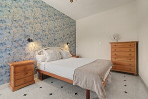 A bedroom with a bed, wooden nightstands, a dresser, and a wall with a floral pattern.