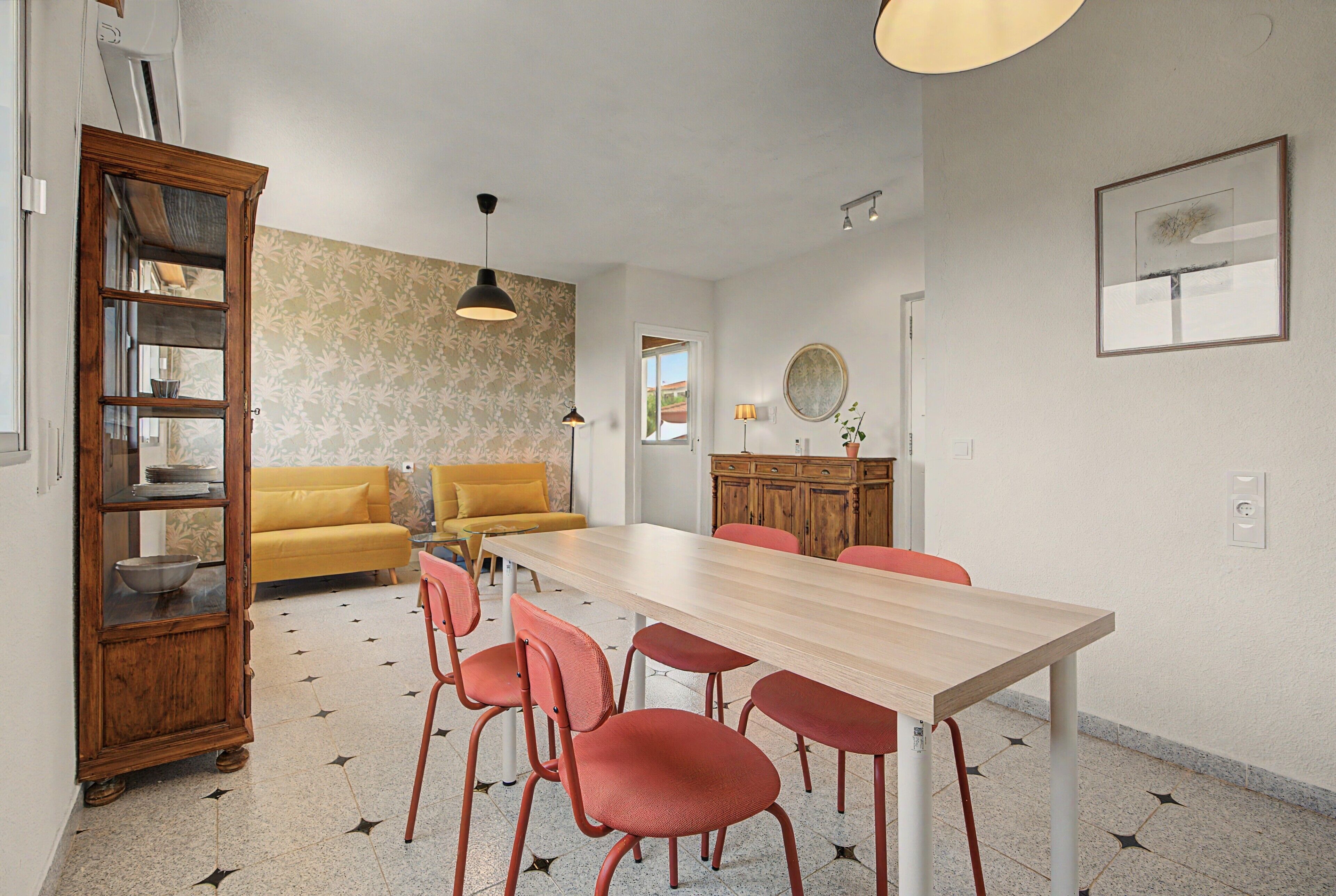 A dining area with a wooden table, red chairs, a yellow sofa, and a cabinet with glass doors.