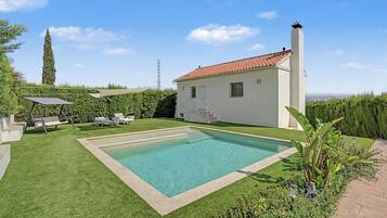 Una casa con piscina, un patio techado con sillas y vistas al campo.