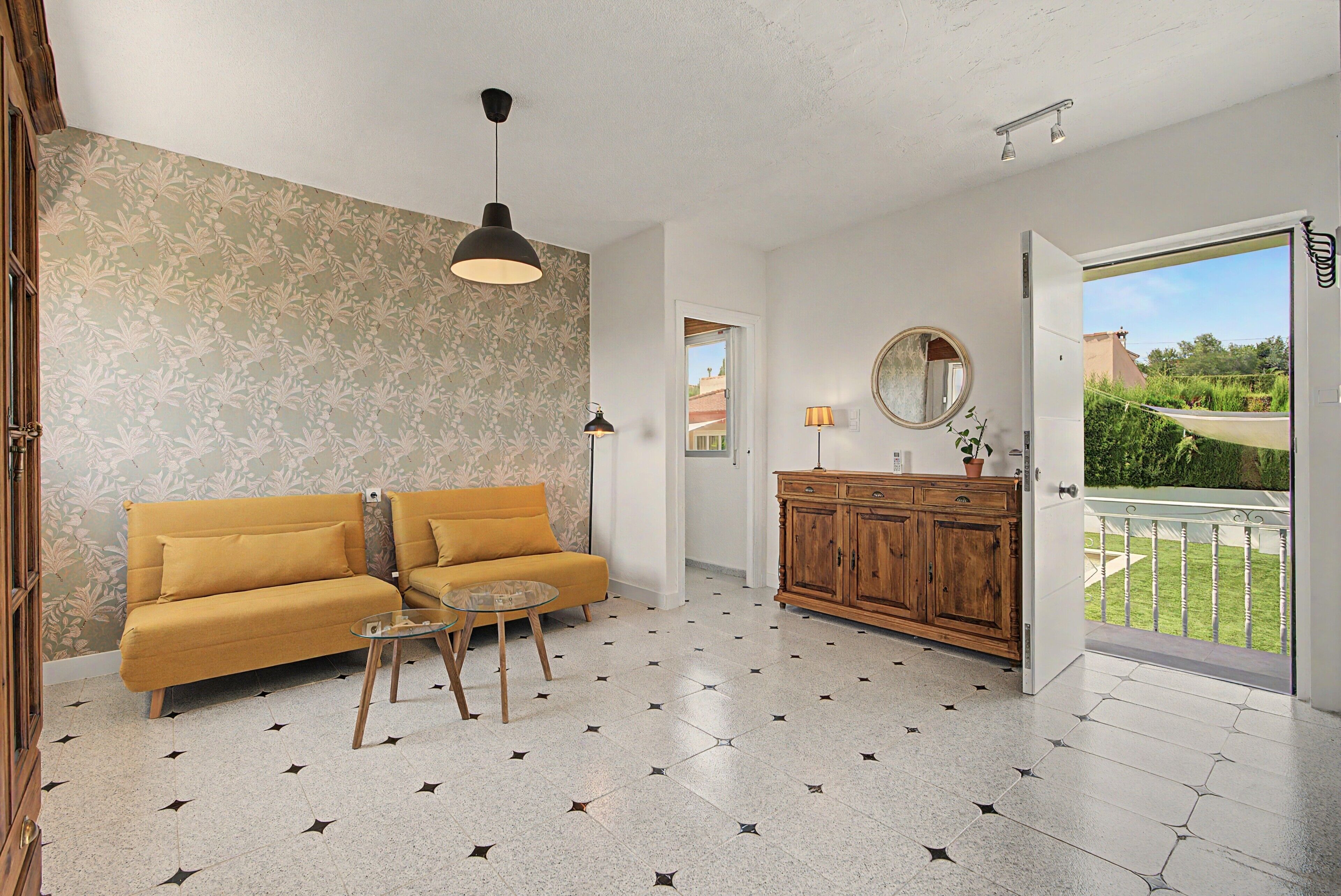 Een woonkamer met een bank, een glazen salontafel, een houten kast en uitzicht door een open deur op een balkon.