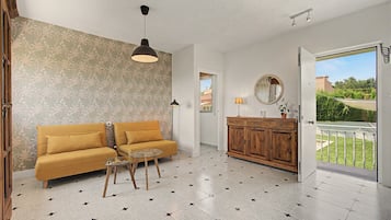 Een woonkamer met een bank, een glazen salontafel, een houten kast en uitzicht door een open deur op een balkon.