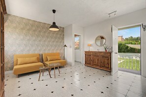 Un salon comprenant un canapé, une table basse en verre, un meuble en bois et une vue sur un balcon, accessible par une porte ouverte.