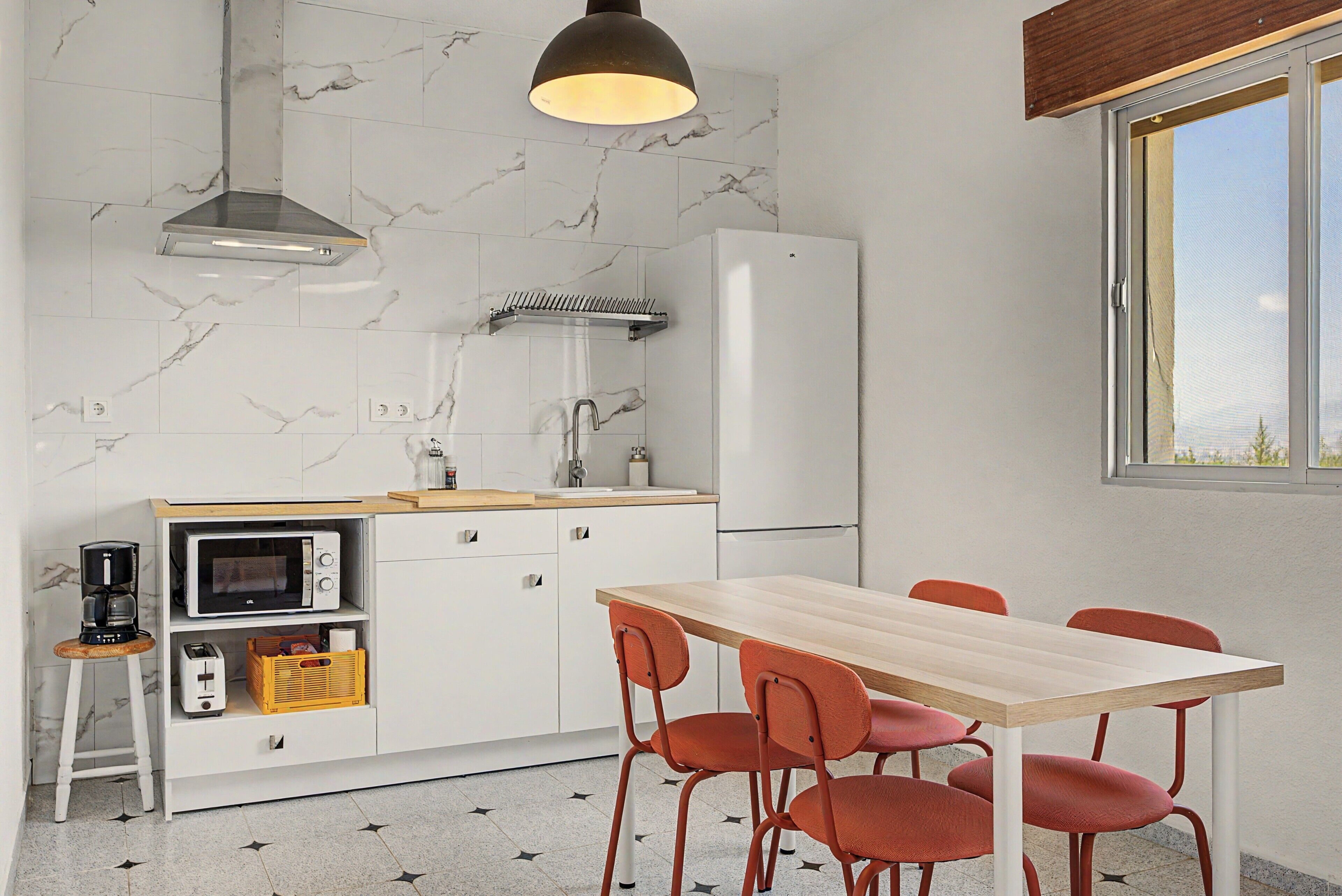 A compact kitchen with a dining area, a built-in oven, a coffee maker, and a window providing natural light.