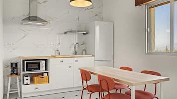 A compact kitchen with a dining area, a built-in oven, a coffee maker, and a window providing natural light.