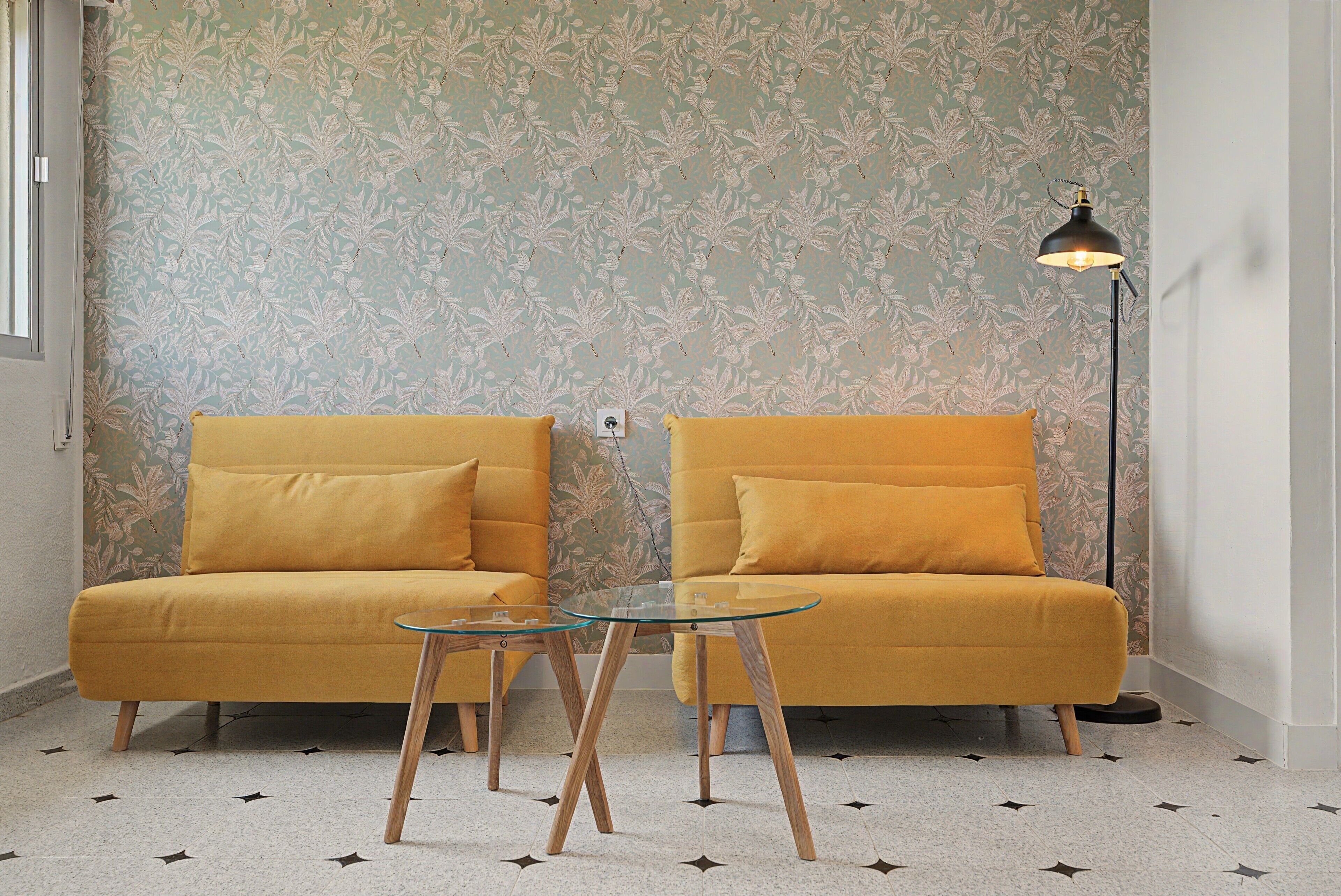 A room with two mustard-colored sofas, a glass coffee table, and a floor lamp.