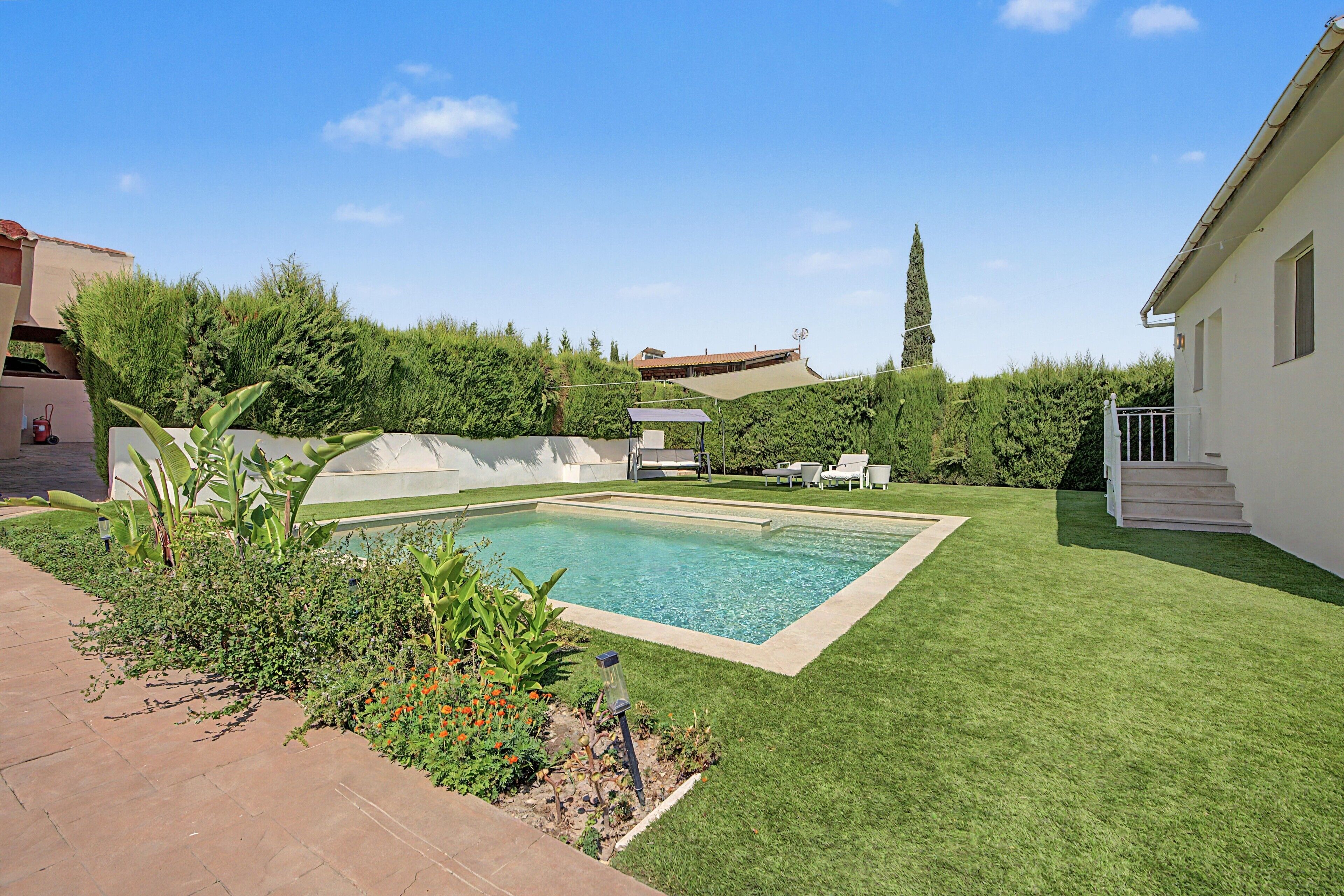 Una piscina rectangular con una zona verde circundante y un edificio blanco con balcón.