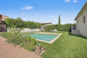 A rectangular swimming pool with a surrounding grassy area and a white building with a balcony.