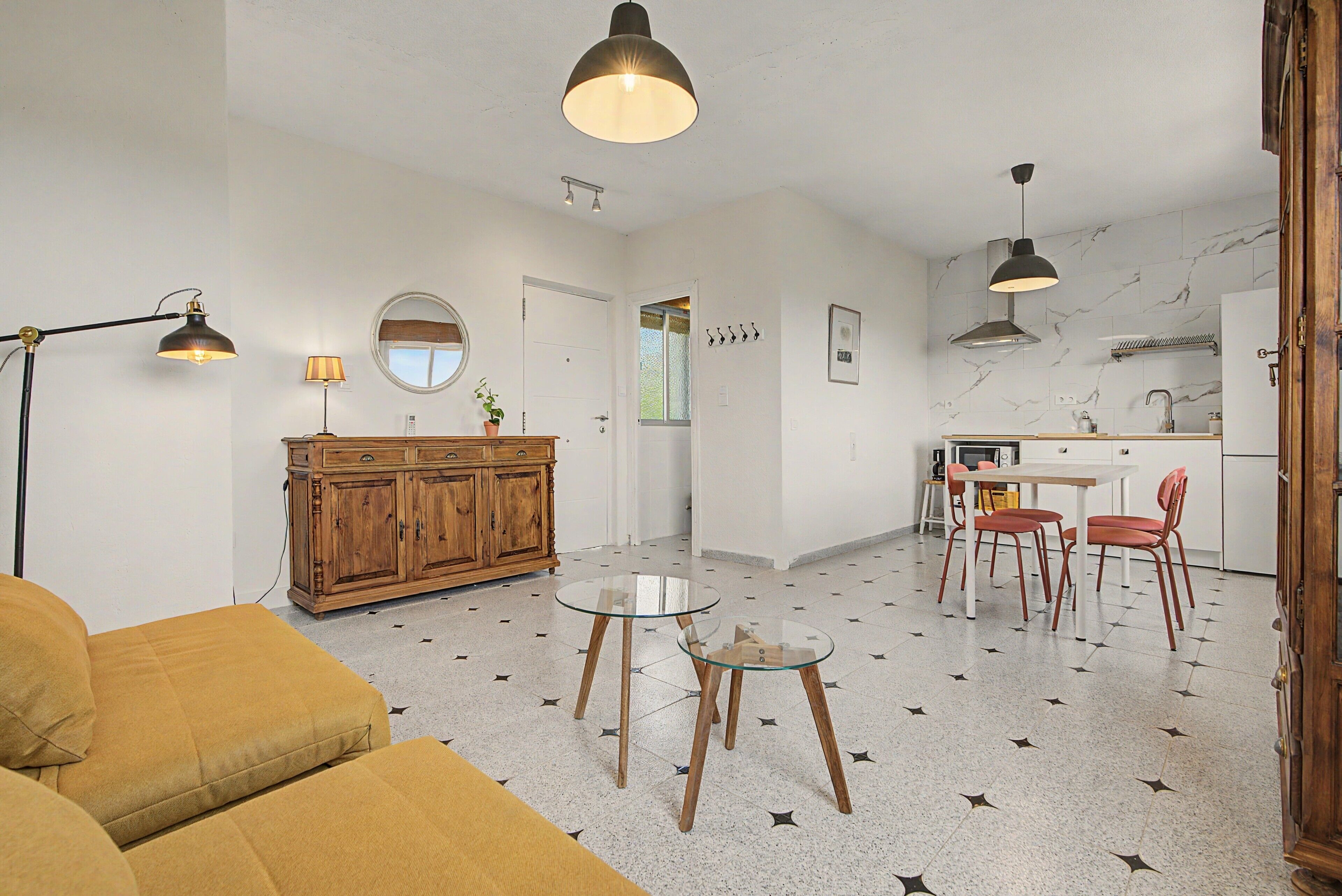 Una sala de estar con sofá, una mesa de centro de vidrio y un comedor con sillas y una mesa.