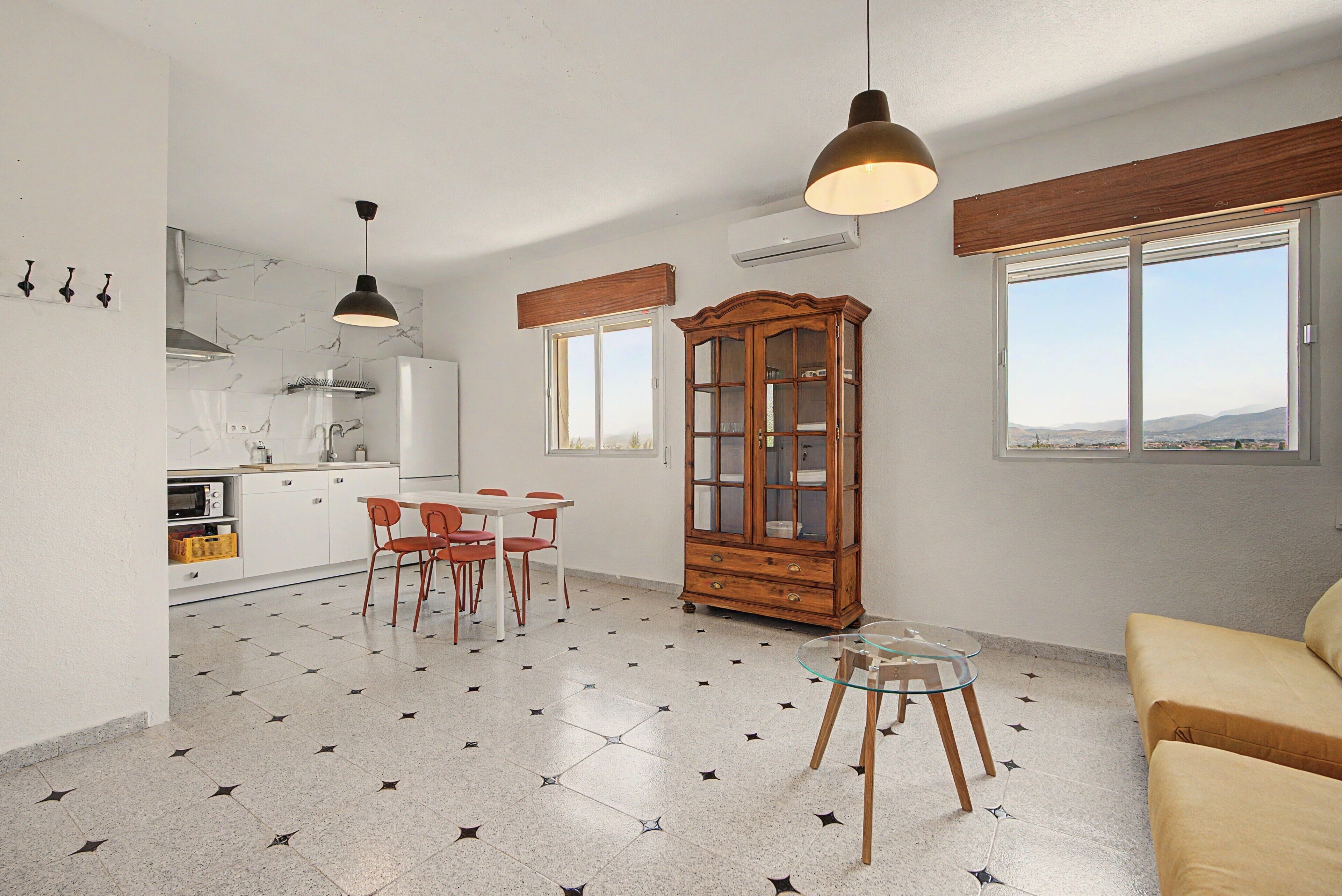 A modern kitchen with a dining area, a wooden cabinet, and a view through the window.