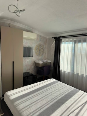 A hotel room with a bed, a desk with a chair, a wardrobe, a mirror, and a window with curtains. - Gelibolu Port Pansiyon (Gelibolu)