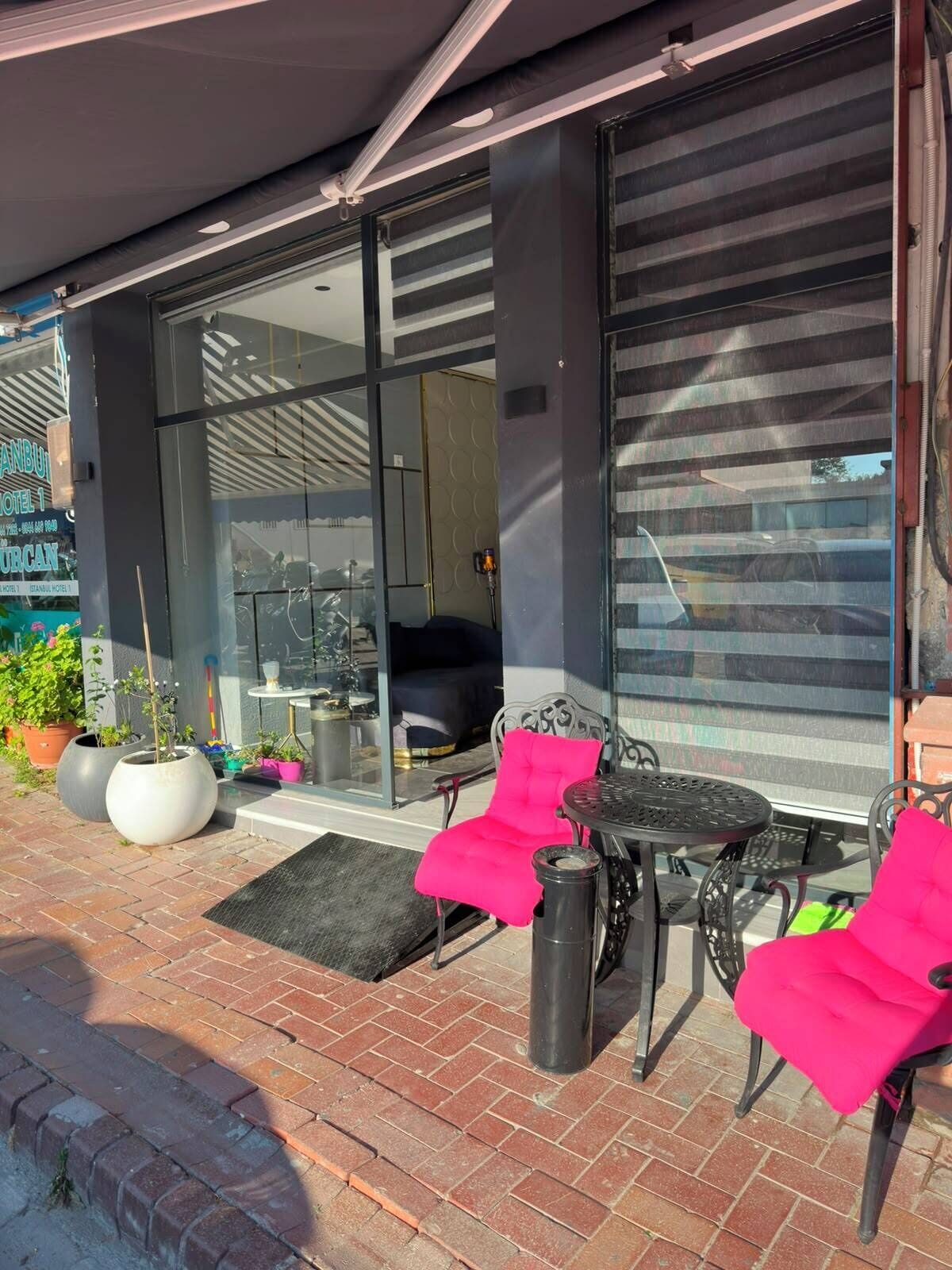Un espace extérieur moderne, aménagé avec une porte d’entrée en verre, des plantes en pot et une table et des chaises en métal.