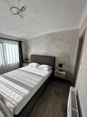 A modern bedroom with a large bed, bedside tables, a radiator, and a decorative wall. - Gelibolu Port Pansiyon (Gelibolu)