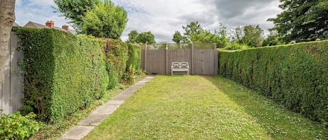 A backyard with a wooden fence, a white bench, and a hedge.