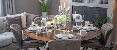 Mesa de comedor lista con platos blancos, tazas y cubiertos, rodeada de sillas de cuero.