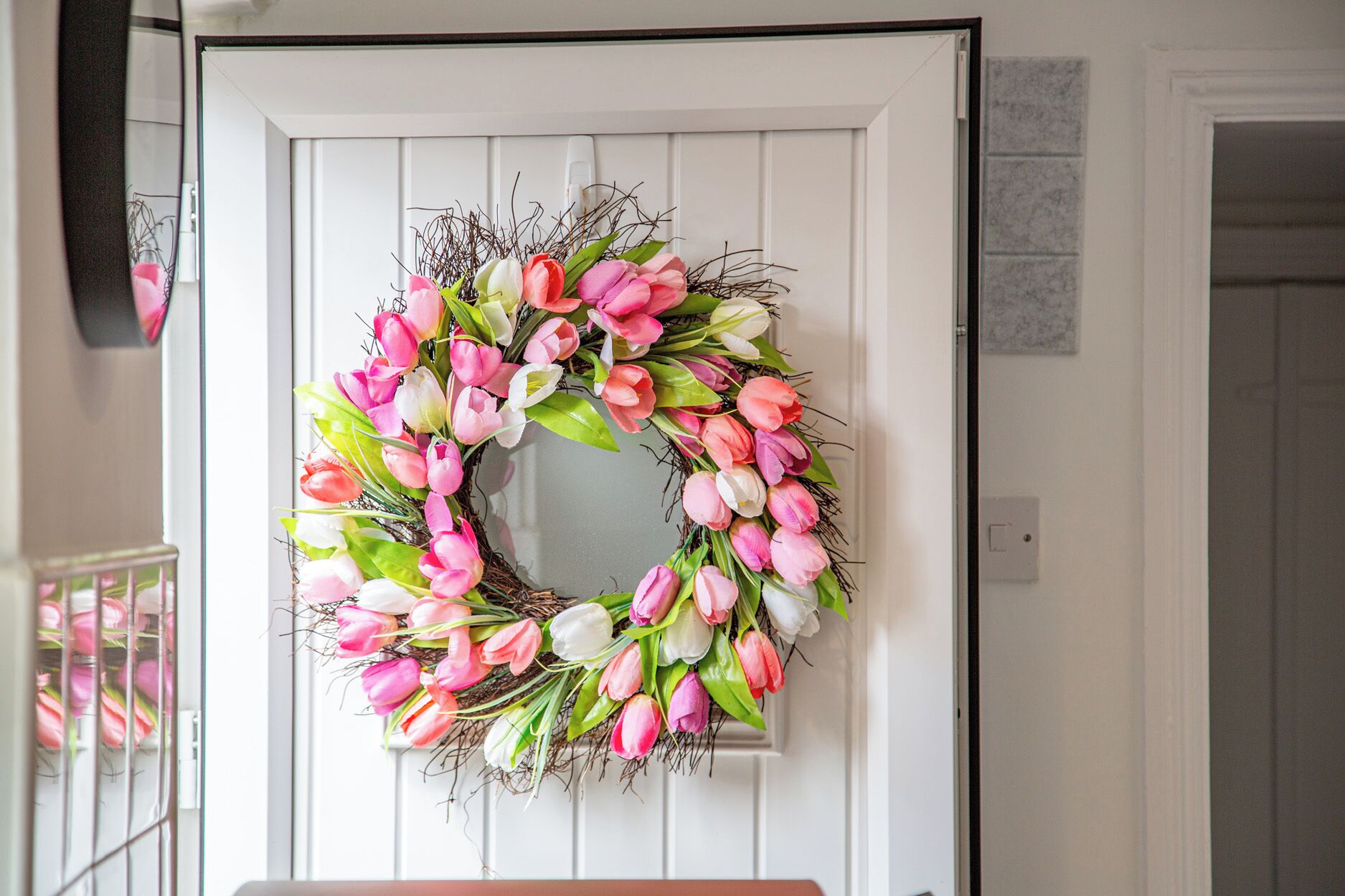 A white door with a wreath of pink and white flowers.