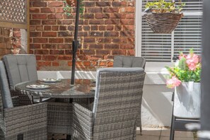 An outdoor seating area with wicker chairs and a table, a brick wall, and a hanging basket with flowers.
