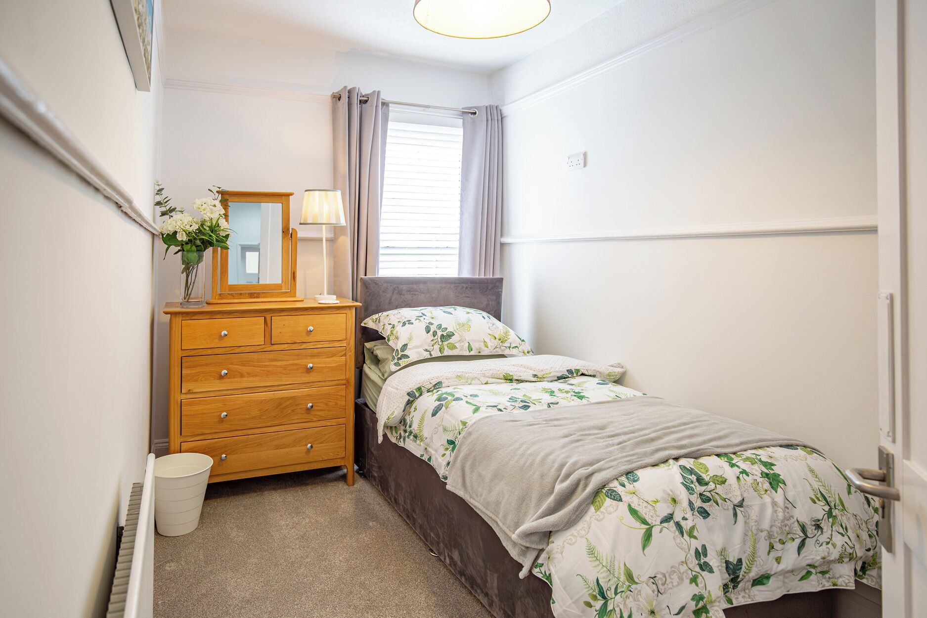 A bedroom with a bed, a dresser, a mirror, a lamp, and a window with curtains.