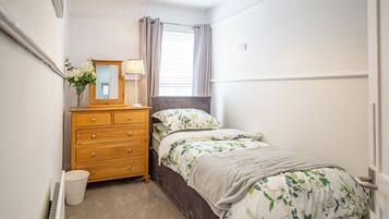 A bedroom with a bed, a dresser, a mirror, a lamp, and a window with curtains.