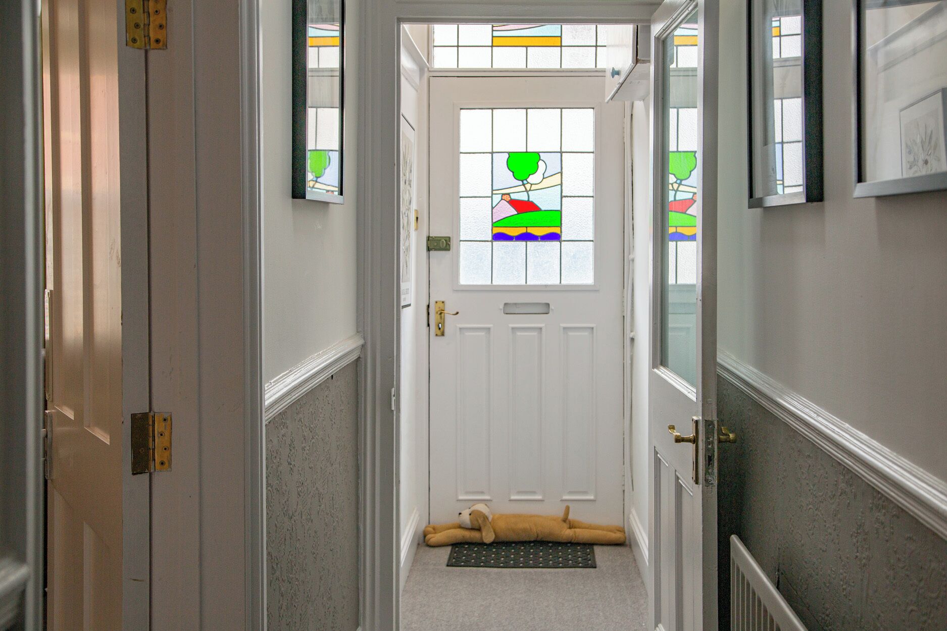 A hallway leading to a door with a doormat and a dog lying on it.