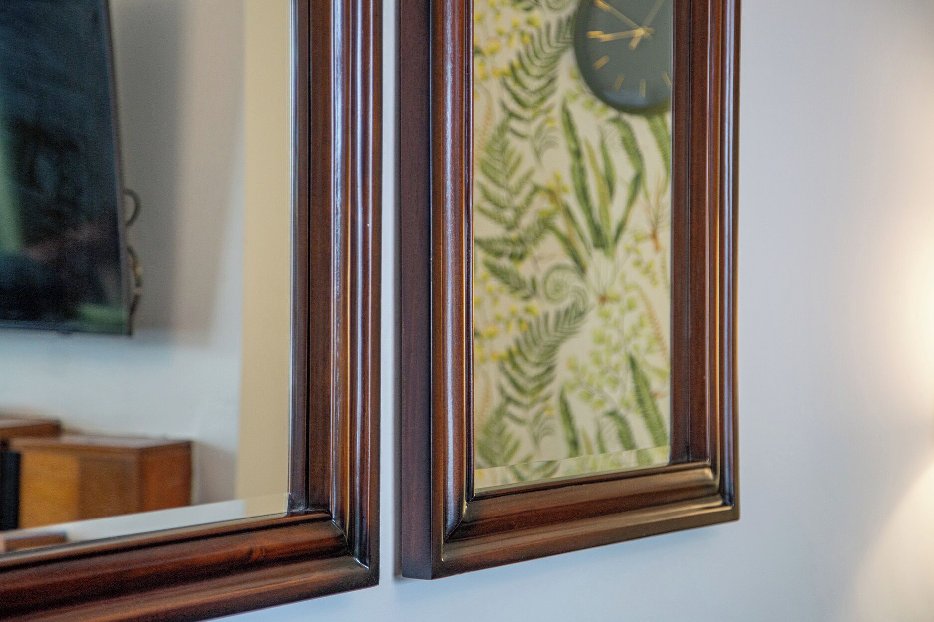 A framed picture with a clock, a mirror, and a patterned wall.