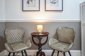 Zwei Ledersessel mit gesteppten Rückenlehnen, ein kleiner Holztisch mit Lampe und gerahmte Pflanzenbilder an der Wand.