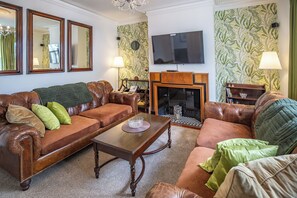 Ein Wohnzimmer mit braunem Ledersofa, einem Holztisch, einem Kamin und einem an der Wand befestigten Fernseher.