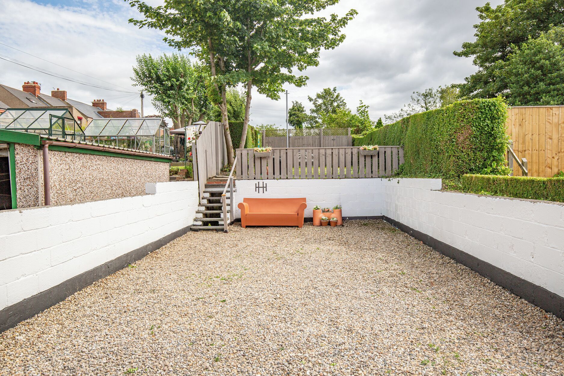 A backyard with a gravel path, a wooden bench, a small staircase, and a wooden fence.