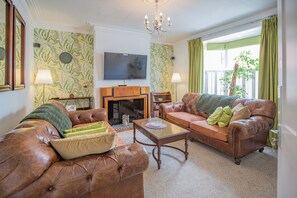 Una sala de estar con chimenea, sofás de cuero, televisor y candelabro.