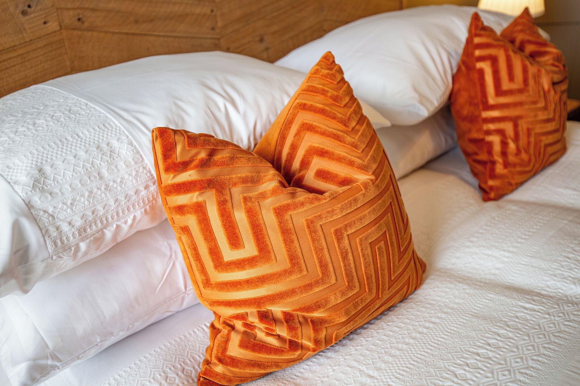 A bed with white bedding and two orange pillows with a chevron pattern.