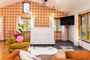 Une pièce avec un mur orné de motifs, un meuble blanc, un canapé, une table basse et un téléviseur.
