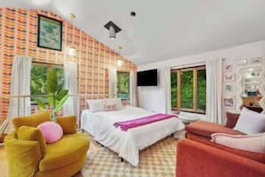 Une chambre à coucher avec un lit, deux chaises, une télévision et une fenêtre.