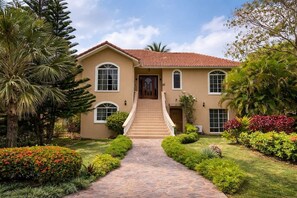 A two-story house with a central staircase leading to the front door, surrounded by well-maintained gardens and palm trees. - Fabulous family-friendly 5-bedroom villa with AC in vibrant Sosúa. (Sosúa)