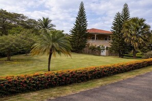 A building with a red-tiled roof, surrounded by a well-maintained lawn and various trees. - Fabulous family-friendly 5-bedroom villa with AC in vibrant Sosúa. (Sosúa)