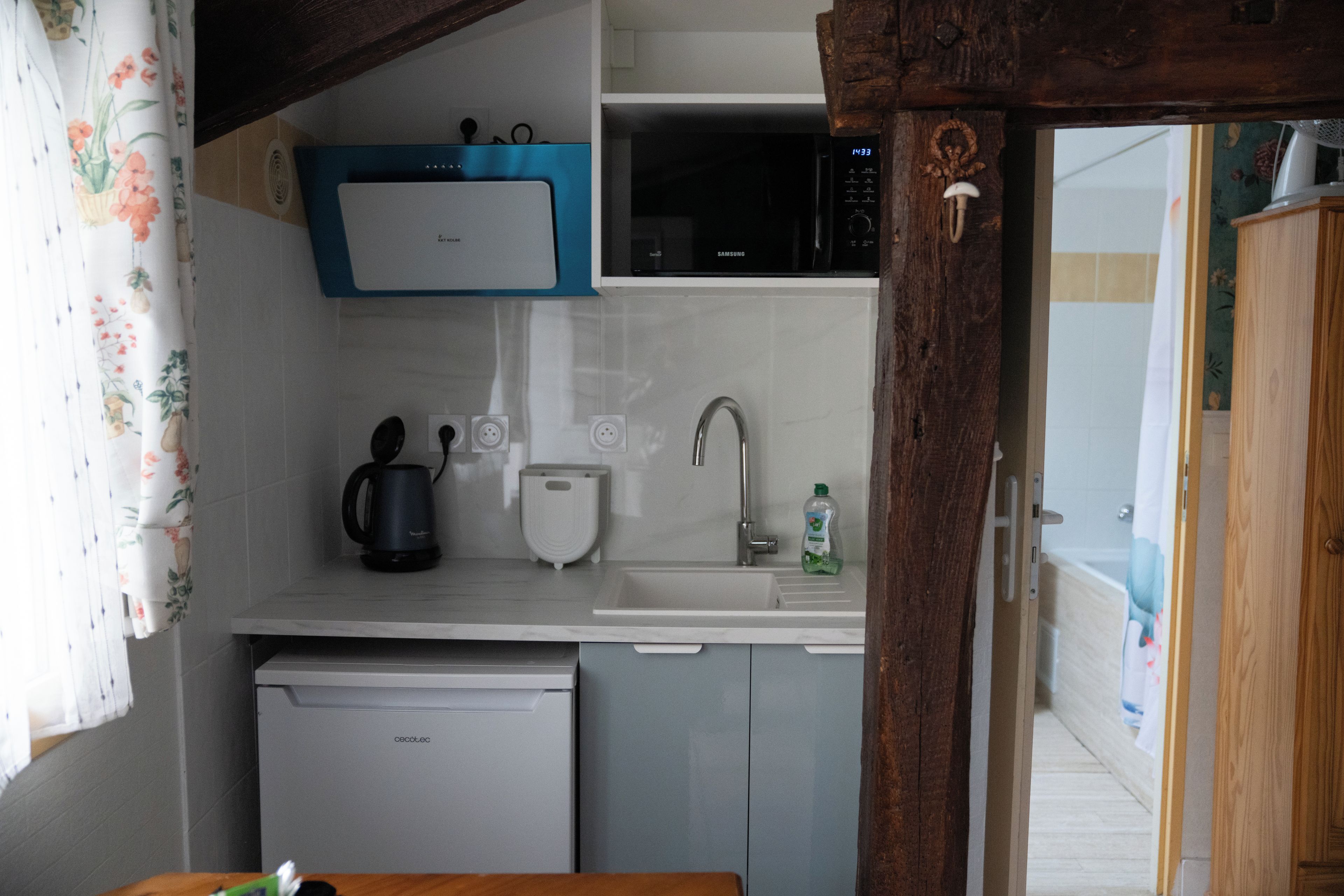 Una kitchenette compacta con microondas, tetera y lavamanos.