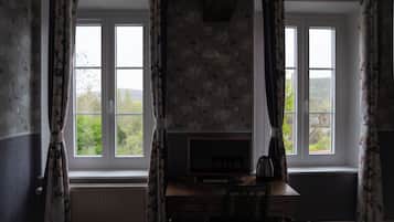 Una habitación con dos ventanas, un radiador, un escritorio de madera con silla y una televisión.