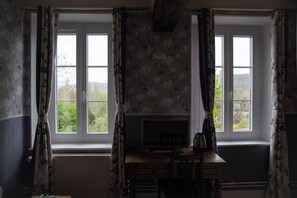 A room with two windows, a radiator, a wooden desk with a chair, and a television.