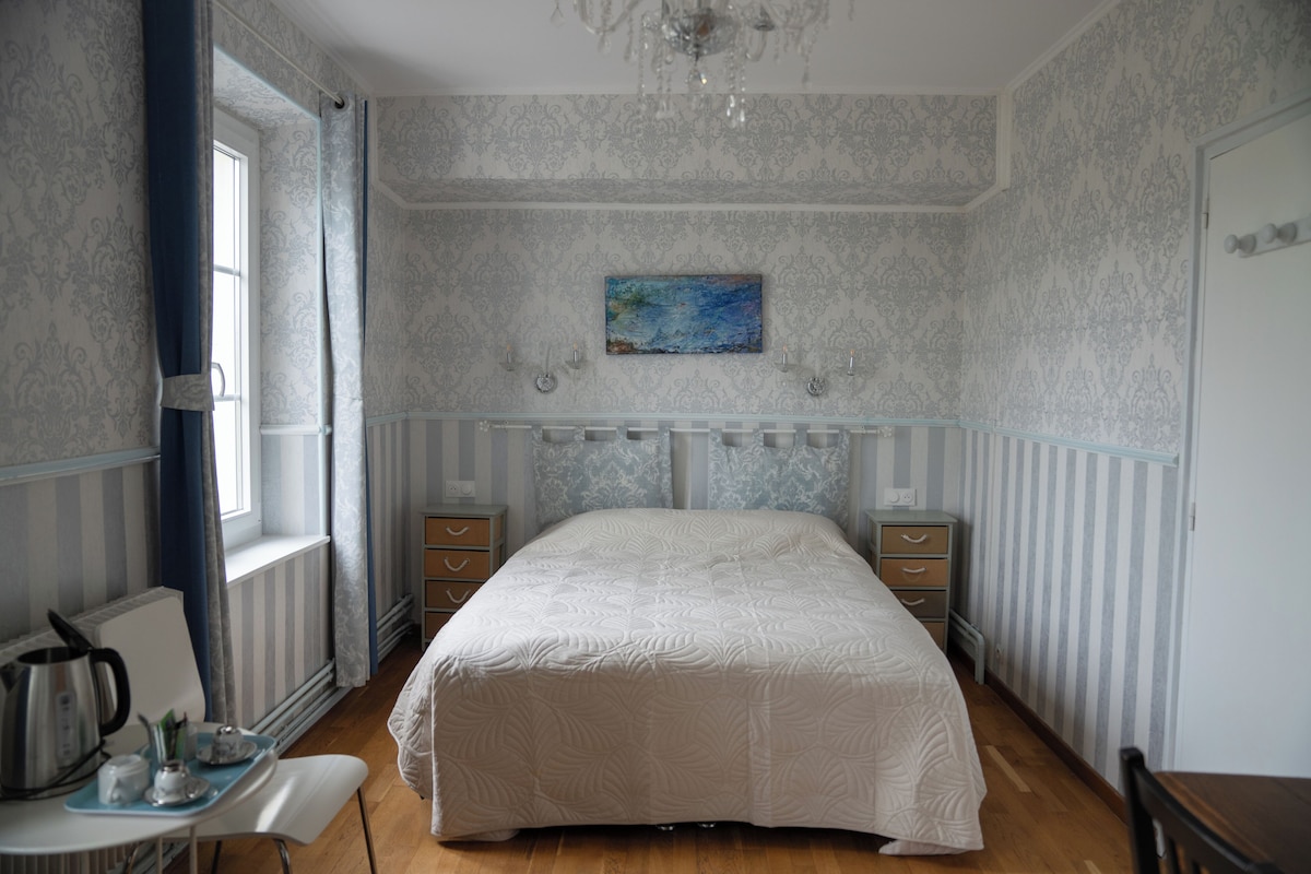 Un dormitorio con una cama grande, un aparador, una silla, una mesa con un hervidor y un cuadro en la pared.
