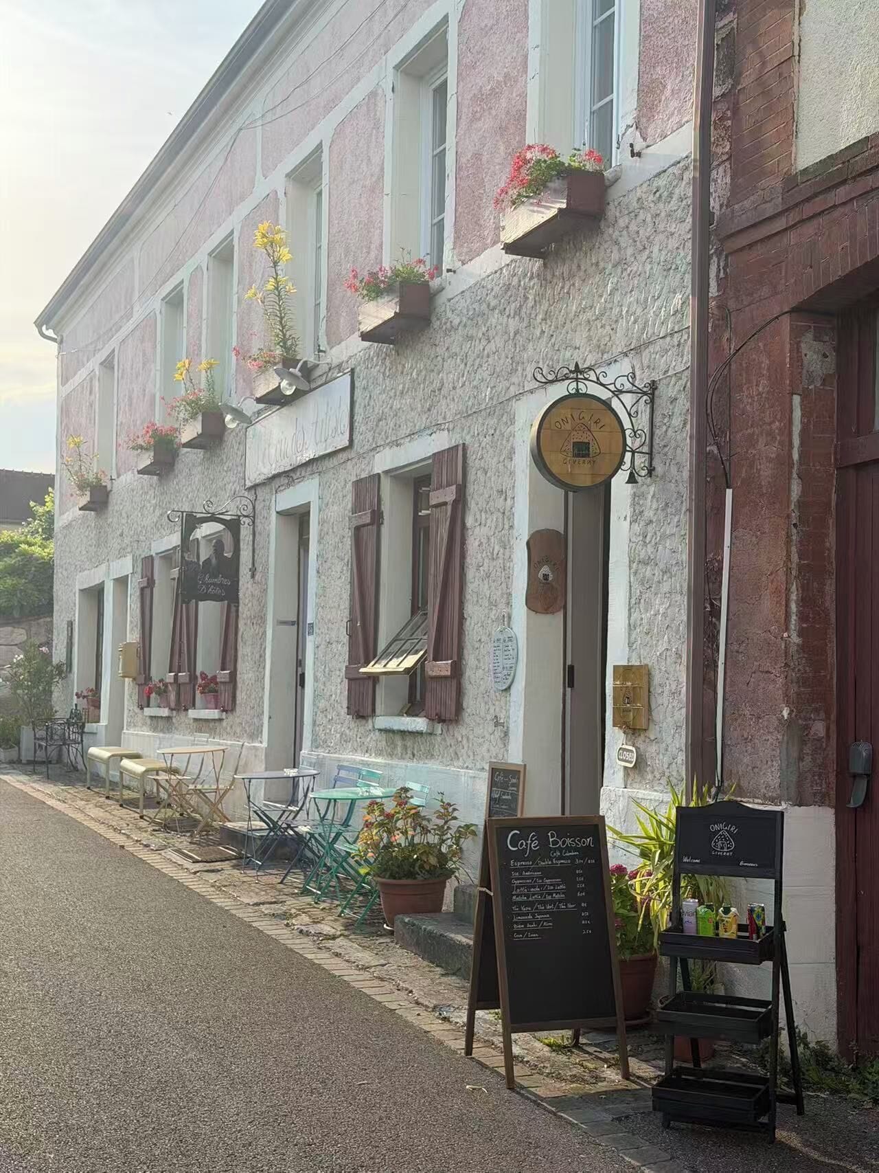 A building with a signboard, outdoor seating, and potted plants.
