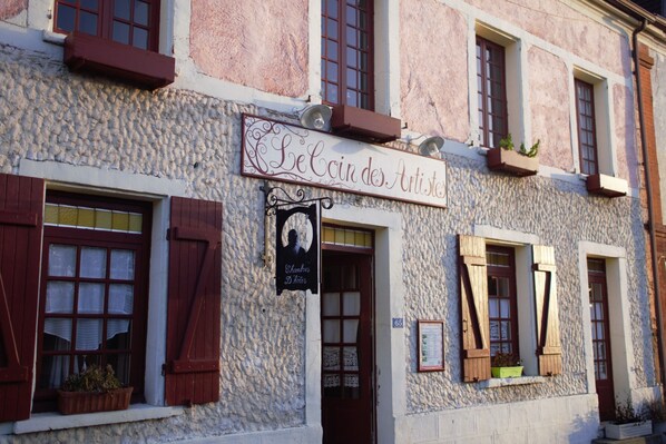 Ein Gebäude mit einem Schild, auf dem 'Le Coin des Artistes' steht, und einem kleineren Schild darunter, das 'Chambres D'Hôtes' zeigt.
