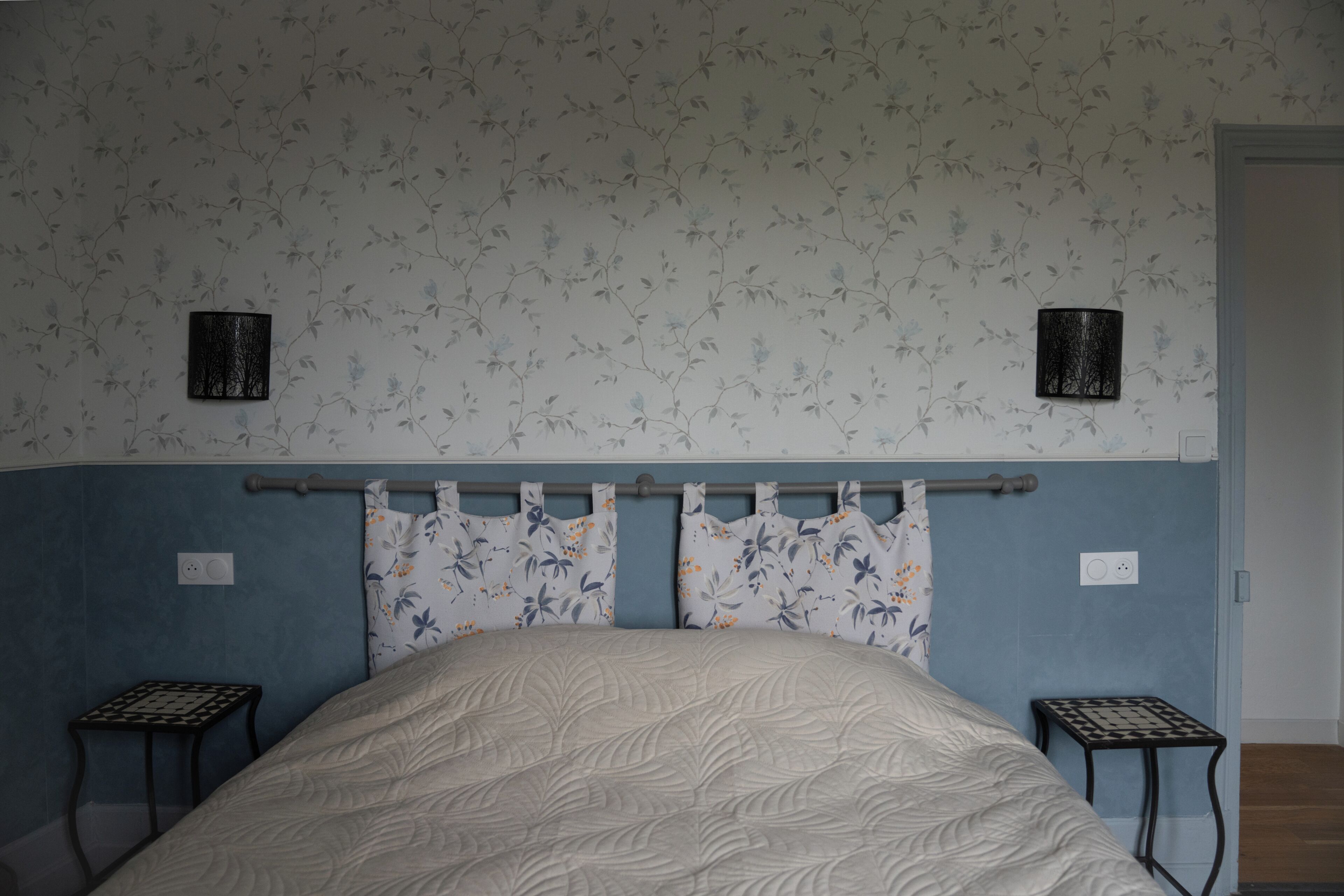 Un dormitorio con una cama, dos mesitas de noche, un cabecero y una pared con papel tapiz floral.