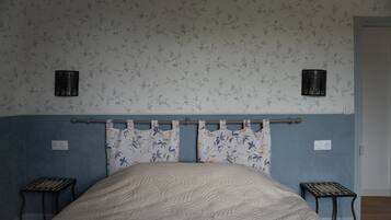Un dormitorio con una cama, dos mesitas de noche, un cabecero y una pared con papel tapiz floral.