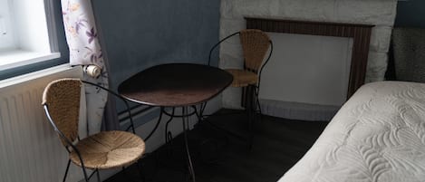 Ein Zimmer mit einem Bett, einem Kamin, einem Tisch und zwei Korbstühlen.