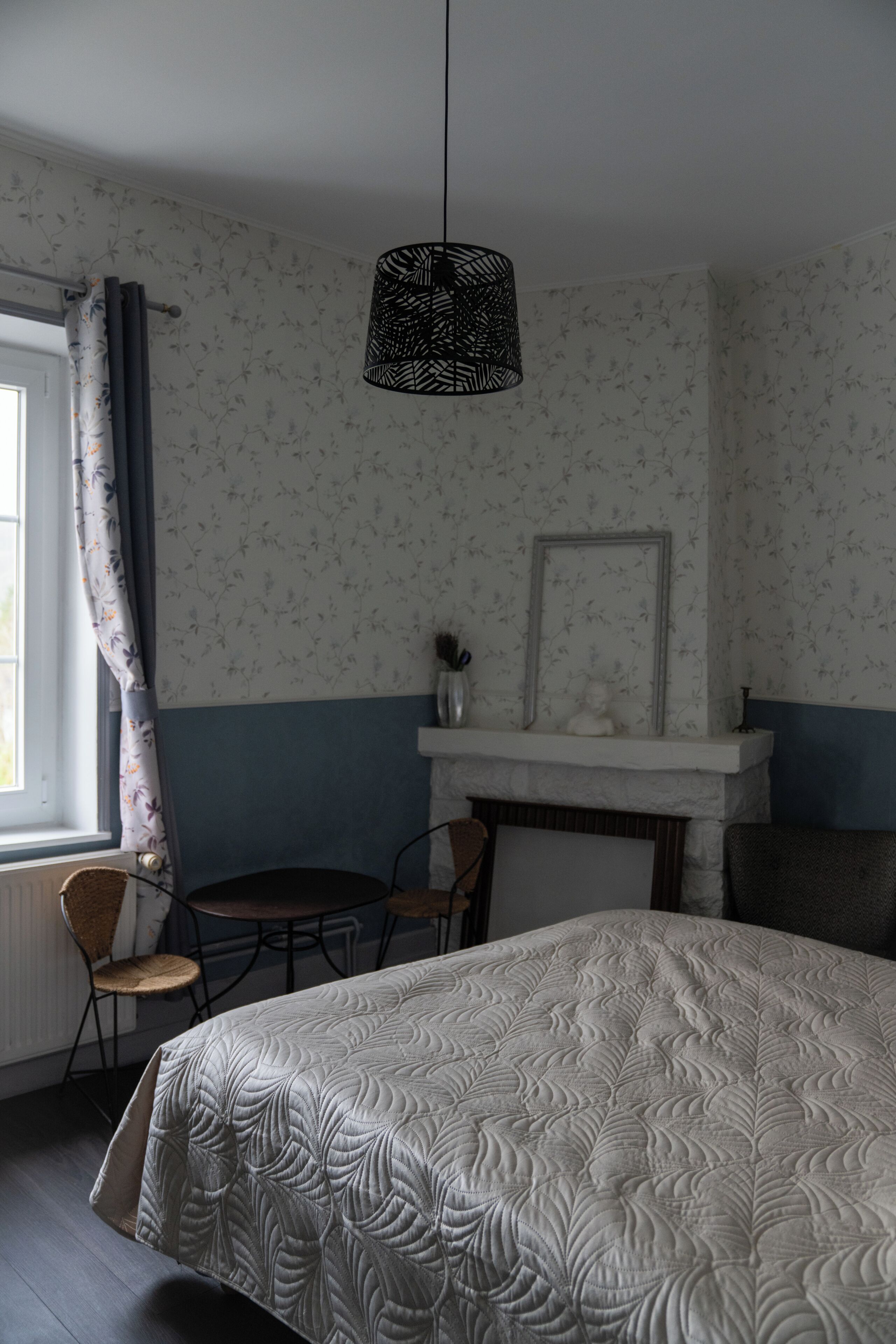 Une chambre à coucher comprenant un lit, une chaise, une table, un luminaire suspendu et une cheminée.