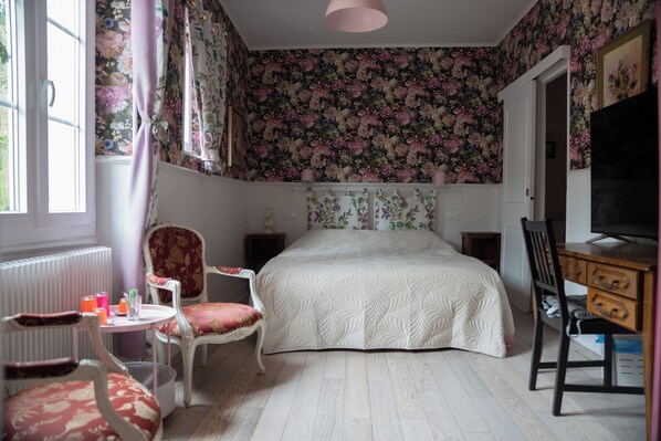 A bedroom with a bed, a chair, a desk, a radiator, and a television.
