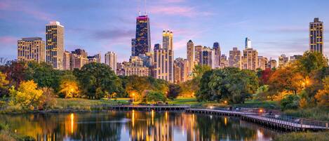 A city skyline with high-rise buildings, a park with trees, and a calm lake reflecting the buildings.