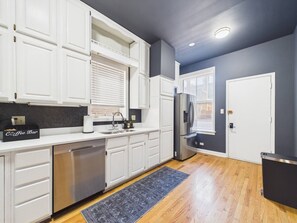 A modern kitchen with white cabinets, a stainless steel refrigerator, and a coffee bar.