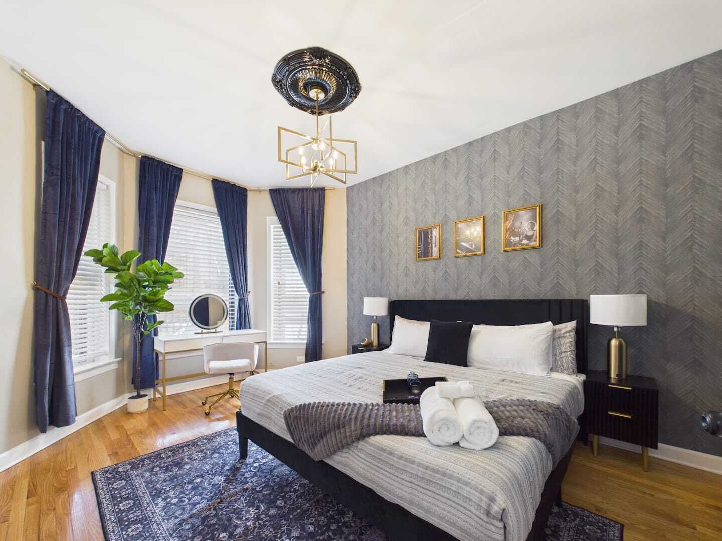 Ein modernes Schlafzimmer mit einem Bett, Nachttischen, einem Schreibtisch und einem großen Fenster mit Vorhängen.