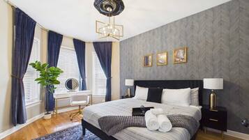 A modern bedroom with a bed, bedside tables, a desk, and a large window with curtains.