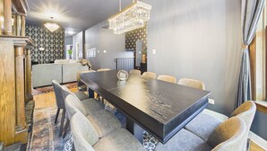 Uma área de refeições moderna com uma mesa comprida, cadeiras acolchoadas, um lustre e uma parede com padrão.