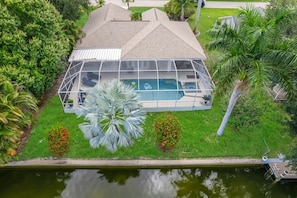 A house with a swimming pool, surrounded by lush greenery and a body of water.